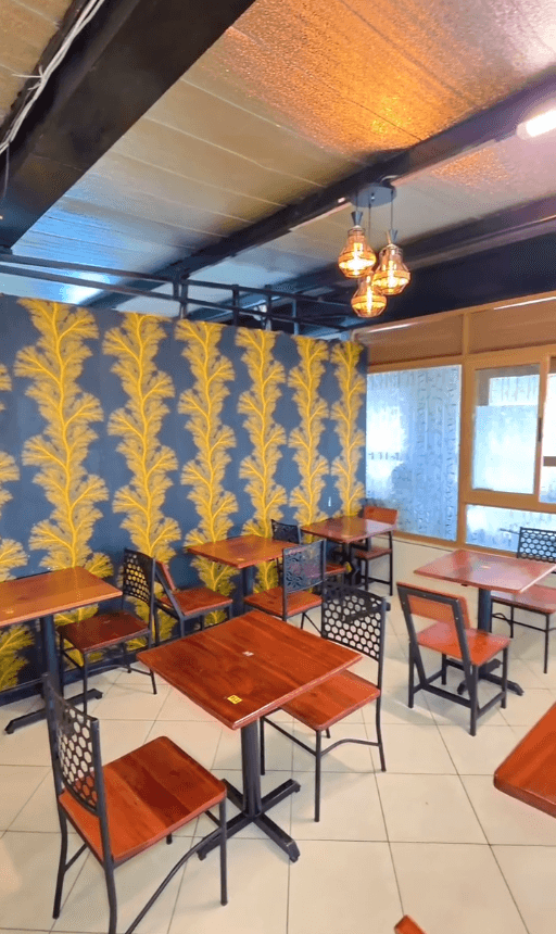 The Hive Pastries rooftop branch — wood tables and black metal chairs against a yellow-and-blue botanical feature wall