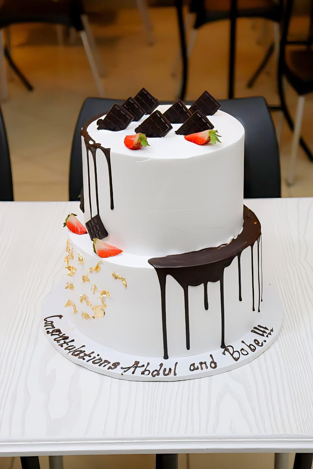 Two-tier white cake with asymmetric chocolate drip, gold leaf and strawberries