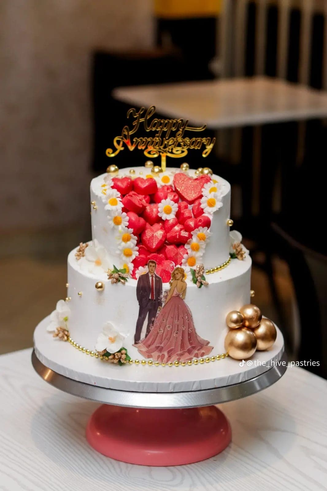 Two-tier anniversary cake with red glitter hearts, daisies and a couple illustration