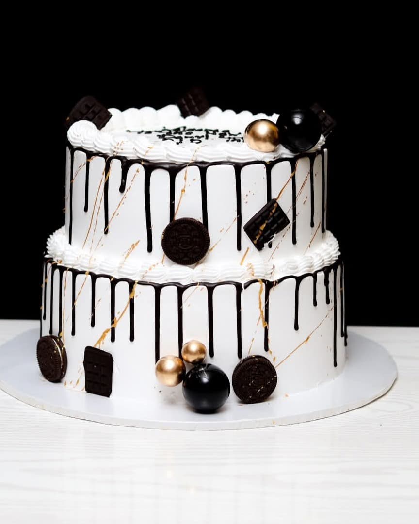 Two-tier white cake with black chocolate drip, gold splash and gilded spheres